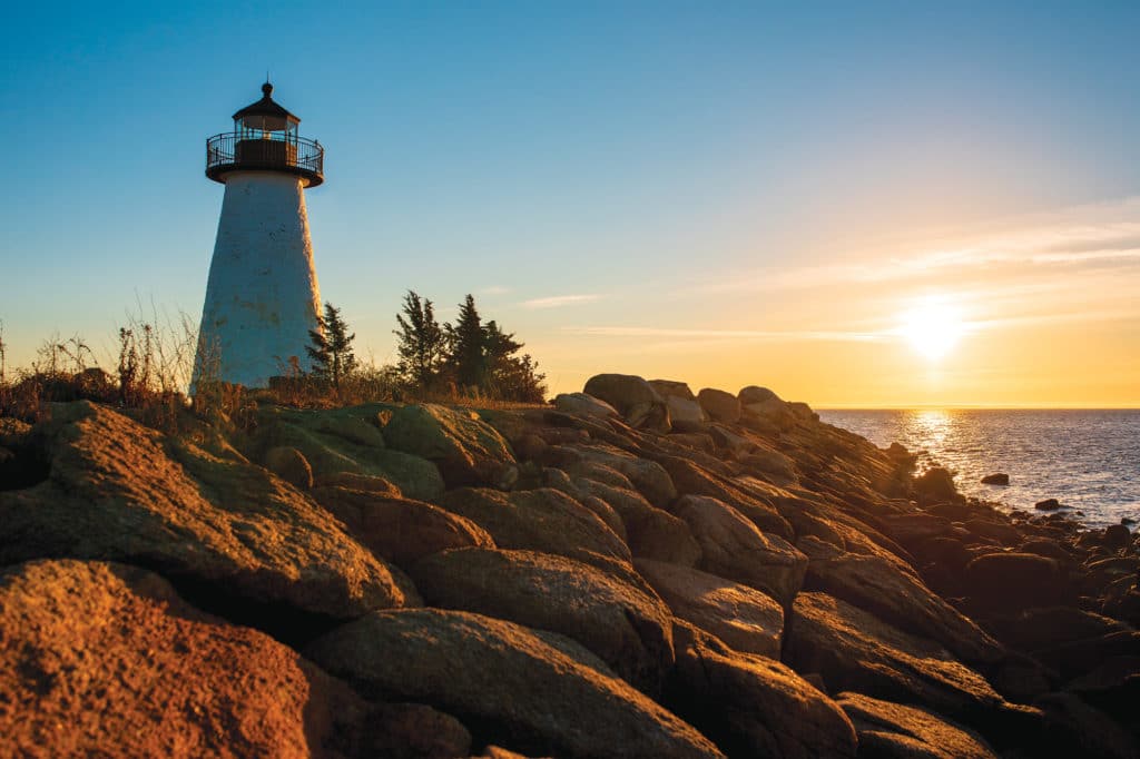 A lighthouse overlooking a rocky shore during a sunset